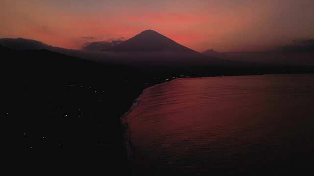 Drone aerial view of Amed Beach in Bali, Indonesia at sunset twilight with Mount Agung volcano visible in the background.