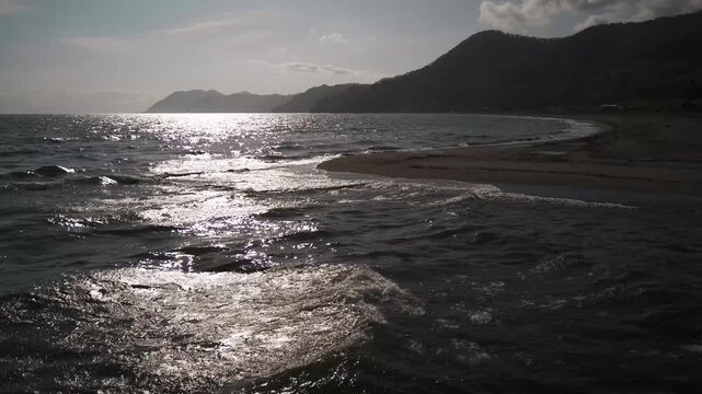A sandbar at a river mouth flowing into a bay, with the silhouette of distant mountain ranges in the background