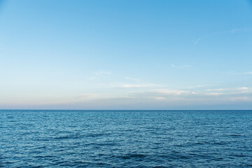 Fototapeta premium A serene view of the calm ocean with a clear blue sky and soft horizon in Italy, perfect for summer vacation themes. The tranquil seascape offers a peaceful and relaxing.