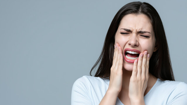 Toothache Pain: A young woman grimaces in pain, clutching her jaw and grimacing as she suffers from a severe toothache.
