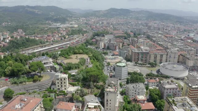 La Spezia, Italy. Aerial flight over the harbor with a massive cruise liner docked at the port, the circular Cathedral of Christ the King, and terracotta rooftops spreading toward the Ligurian Sea. D