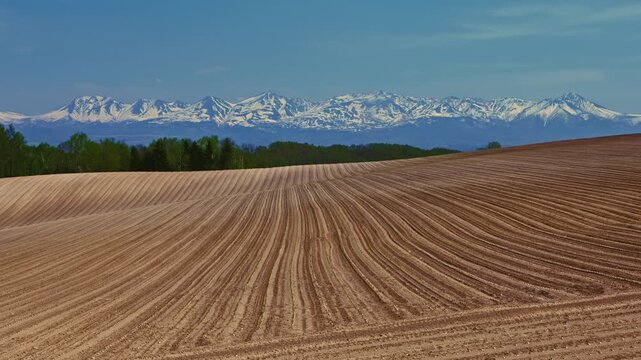 Spring plowed field and snow-covered Tokachi mountain range