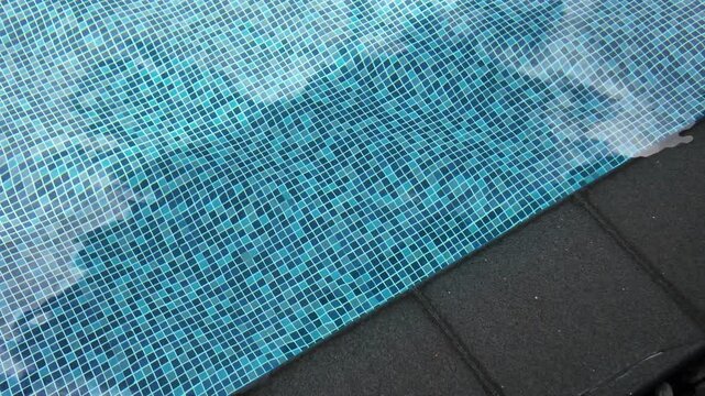 Top view of swimming pool with blue mosaic tiles and water ripples