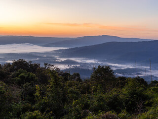 Obraz premium Misty sunrise over Phu Suan Sai National Park, Thailand. Lush green forest in the foreground with foggy mountains. Serene morning sky with soft light.