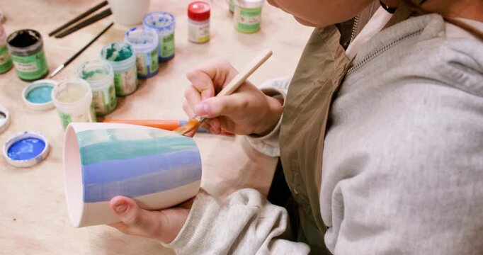 Coloring pottery. Handmade ceramic. Talented child painting on cup using brush developing art skill in artisan professional studio.
