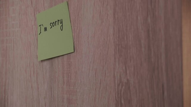 Hand sticking yellow I am sorry sticker on light wood wall. Video footage of requests for forgiveness and conflict resolution.