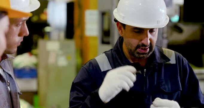 Adult male engineer in hardhat explains production issue during workshop discussion, guiding technical review, inspection planning and decision making for operation near machine line