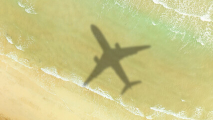 Aerial view of shadow passenger plane silhouette and sandy beach blue sea with waves at sea beach summer vacation sea travel concept	