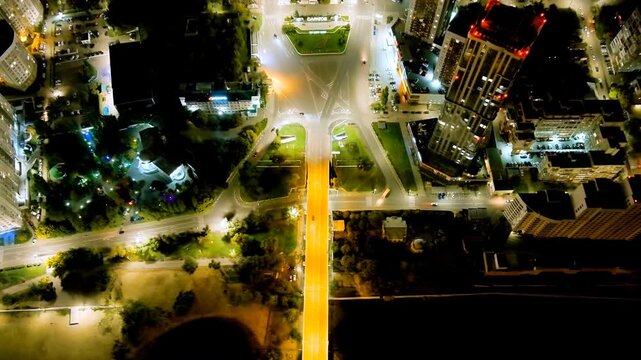Saratov, Russia. Slavyanskaya Square, aerial night panorama with converging illuminated avenues, a prominent high-rise with red warning beacons, and the Volga cityscape stretching to the horizon. Dro