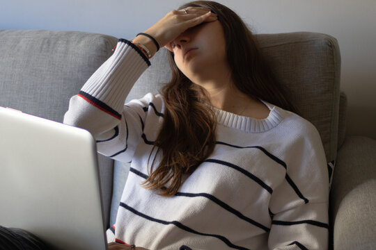 Young woman feeling overwhelmed and stressed from work, covering her face while working remotely on a laptop, struggling with a deadline and experiencing headache and exhaustion
