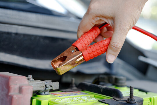 Hand holding jumper cable clamp near car battery