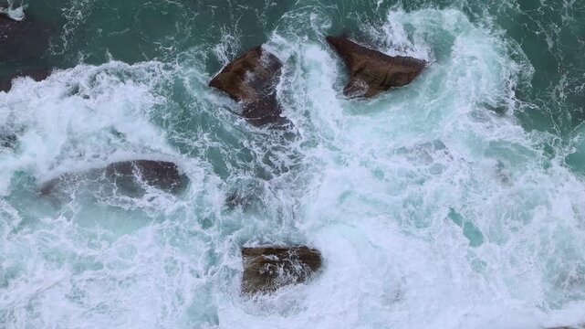White water and waves swirl back and forth and around and over large jagged rocks on the shore, causing mesmerising motion below the ocean bridge at Coalcliff near Sydney in New South Wales, Australia