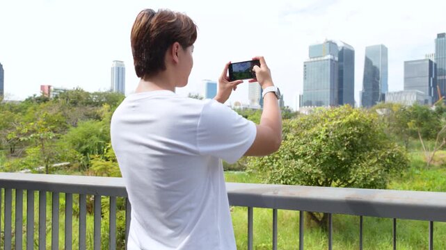 Thai Asian Man Using Smartphone to Capture Bangkok Skyline from Benchakitti Park