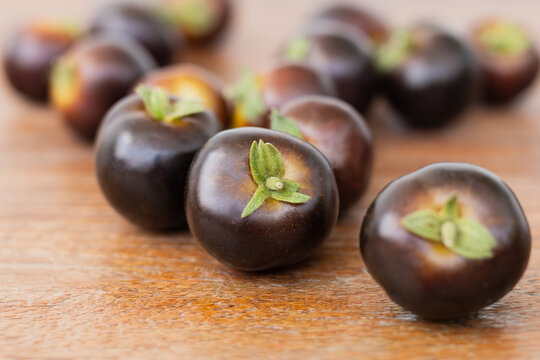Pile of dark purple Indigo Rose cherry tomatoes on wooden table.