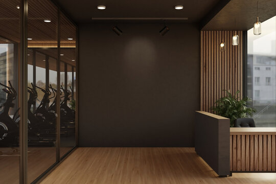 Black wall between glass door of exercise room and reception counter in a modern luxury fitness gym.