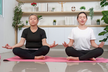 Fototapeta premium Asian senior and young women meditating together at home, mental wellness