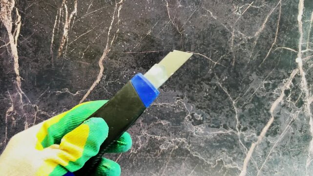 Against a dark background, a hand in a work glove opens and closes a utility knife. Concept of repair, cutting, working tools. High quality 4k footage