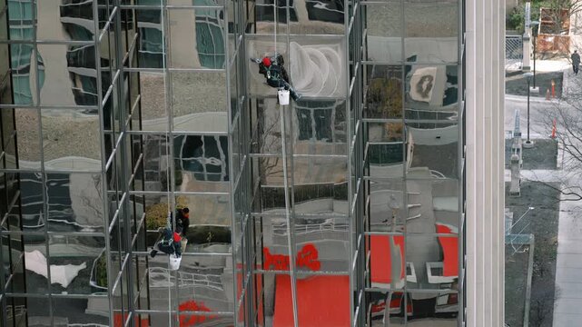 Window cleaners perform safety checks on highrise. Two professionals manage safety on frosty building exterior