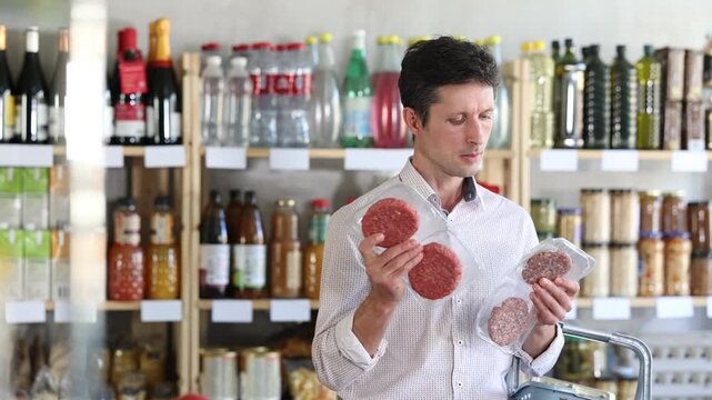 Man in light shirt choose and buy raw cooled semi-finished hamburger cutlet in store. Visitor make choice of assortment, buy raw minced meat product. Customer read label, examine packaging 