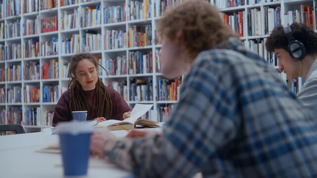Young female student reading a book while studying with classmates in a university library