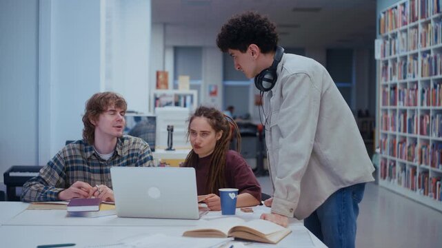 University friends brainstorm and plan their next steps with papers spread across the wooden table. Laughter and serious discussion mix as they solve problems together in a warm library environment.