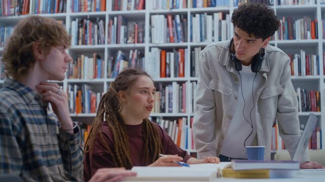 Diverse young learners combine their skills and knowledge while researching and writing for a team project. The university library provides a calm backdrop with natural light and rows of books.