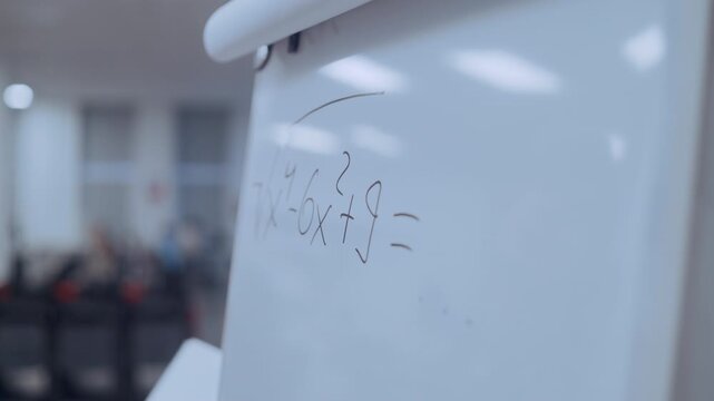 Close-up of a hand writing a complex mathematical formula on a whiteboard during a lesson