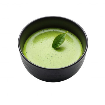 A single fresh green tea leaf floating in a bowl of frothy, bright green matcha tea, isolated against a solid black background