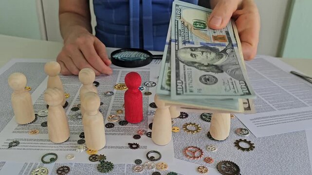 A businesswoman holds a stack of cash above a group of wooden figurines arranged on a table littered with gears and papers. Decision making, discussion, and the distribution of income in society