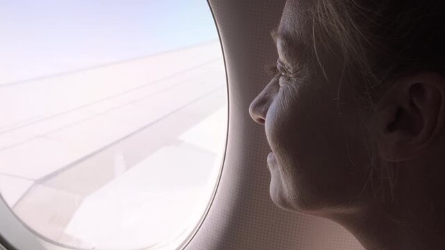 Happy woman passenger looking out airplane window during flight