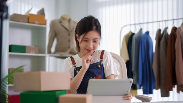 young Asian women entrepreneur live streaming selling products online merchant small business owner using tablet computer managing ecommerce store at home
