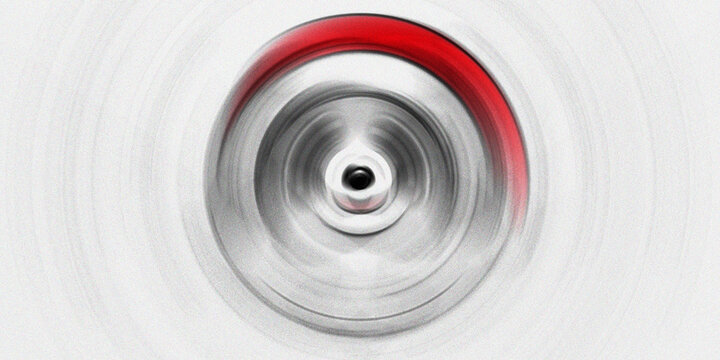 Radial motion blur of circular metallic object with red accents creating dynamic spin effect on light grey textured background.