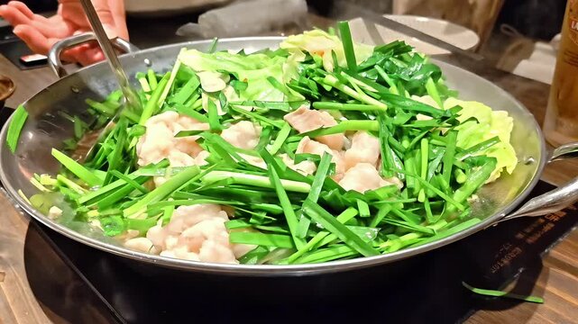 Stirring cooking motsunabe hot pot with chive and chili pepper garnish, Japanese Fukuoka Cuisine Comfort Food, Tender Beef Tripe, Smoky Steaming Miso Broth