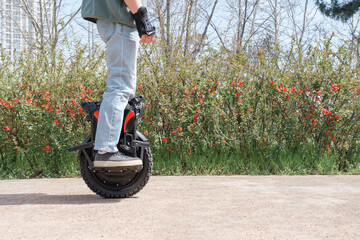 A man in blue jeans and sneakers rides an electric unicycle in park, side view. © TATIANA KIM