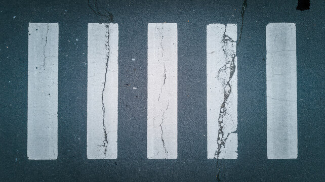 Top down photo of white painted pedestrian crosswalk stripes on cracked asphalt road surface captured in a clear daylight shot