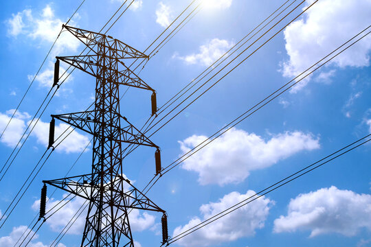 High Voltage Power Lines Against a Bright Blue Sky with Fluffy White Clouds on a Sunny Day