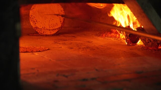 Close up of a baker using a metal tool to remove crispy handmade Matzah from a burning wood-fired oven; traditional Passover Matzah baking process in a Jewish bakery.