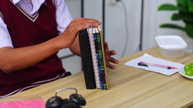 Close up of Student in school uniform organizing stack of notebooks and planners on wooden desk