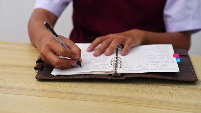 Close-up of Student opening leather binder and using pen to notes on lined paper at wooden desk