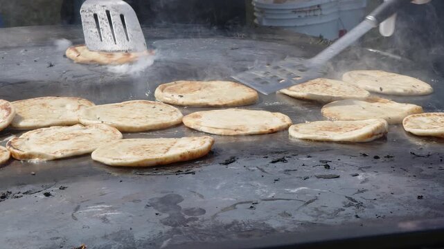 Cooks around huge iron skillet flip naan bread for Indian food festival