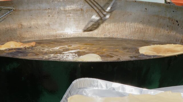 Poori puff bread fries in vat of oil at outdoor Indian food festival