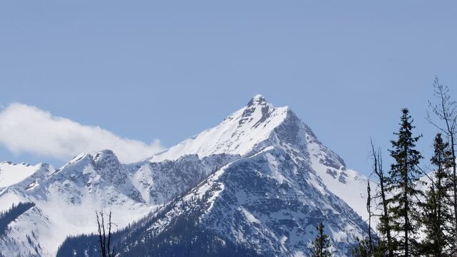 Cloud drifts slowly over rocky mountain peak with snow summit, nature