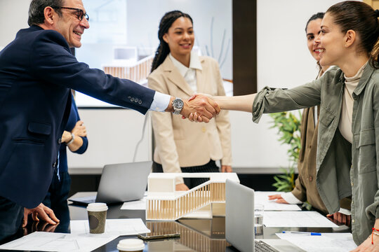 Real estate professionals closing a deal with a handshake, discussing property investments in an office presentation