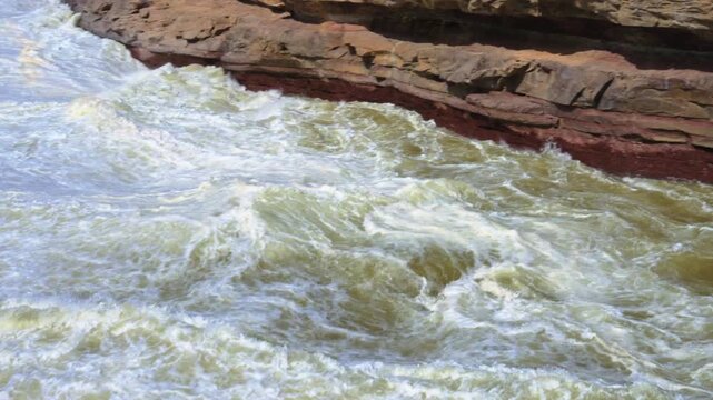 Dynamic panning shot of the Yellow River rapids flowing through the red sandstone gorge at Hukou. Features the turbulent white water and layered sedimentary rock.