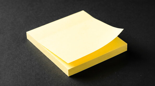 Blank yellow sticky note pad with peeling corner resting on dark textured black background providing empty copy space for office reminder messages