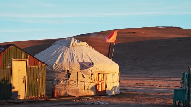 Traditional Kyrgyz yurt and small wooden cabin at sunrise near Song-Kul Lake, Kyrgyzstan, featuring a nomadic campsite in the high-altitude mountain steppe during early morning