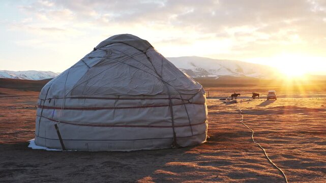 Breathtaking sunrise at a nomadic yurt campsite near Song-Kul Lake, Kyrgyzstan, featuring wild horses grazing in the background of the high-altitude mountain steppe