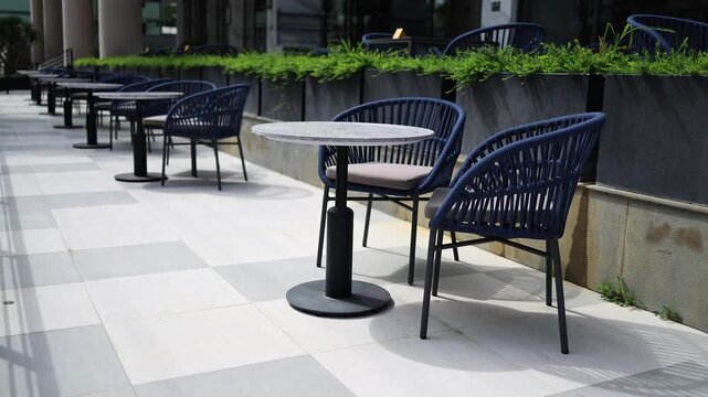 Empty tables and chairs at an outdoor street cafe in Nha Trang, Vietnam. Row of modern blue wicker chairs and round marble tables on a terrace on a sunny day.