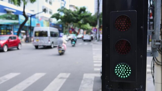 Traffic light close up on a city street with blurred motorbikes and cars moving on a road zebra crossing background. Urban transportation and road safety concept in Nha Trang, Vietnam.