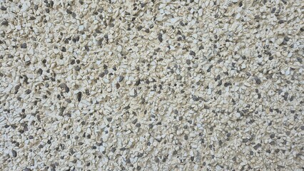 A close-up, full-frame shot showing a rough wall texture covered in small, tightly packed beige and grey stone pebbles embedded in a cement or plaster background. © aura